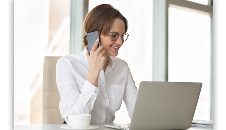 Smiling confident businesswoman making phone call using laptop in office, successful millennial female boss talking on mobile at work, friendly secretary contacting consulting client by cellphone